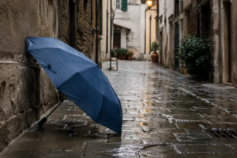 Compact travel umbrella resting against wet stone wall in a European alley