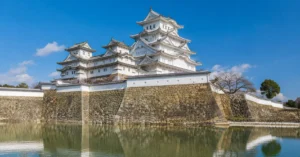 White tiered structure of Himeji Castle rising behind stone defensive walls
