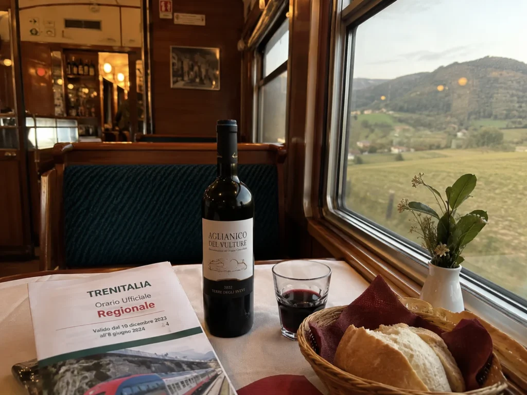 Interior of an Italian regional train with a dining car, timetable, and bottle of wine, showing how you can travel between cities.