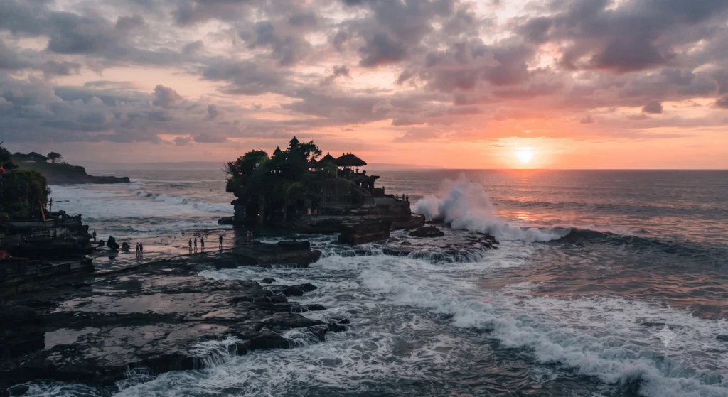 Balinese sea temple on a rocky islet at sunset with waves and visitors on the shore.