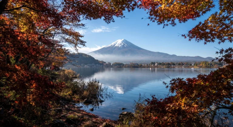 Snow-capped Mount Fuji viewed across Lake Kawaguchiko surrounded by red autumn maple trees