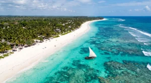White sand beach and turquoise waters along Kenya Coast with traditional dhow boat.